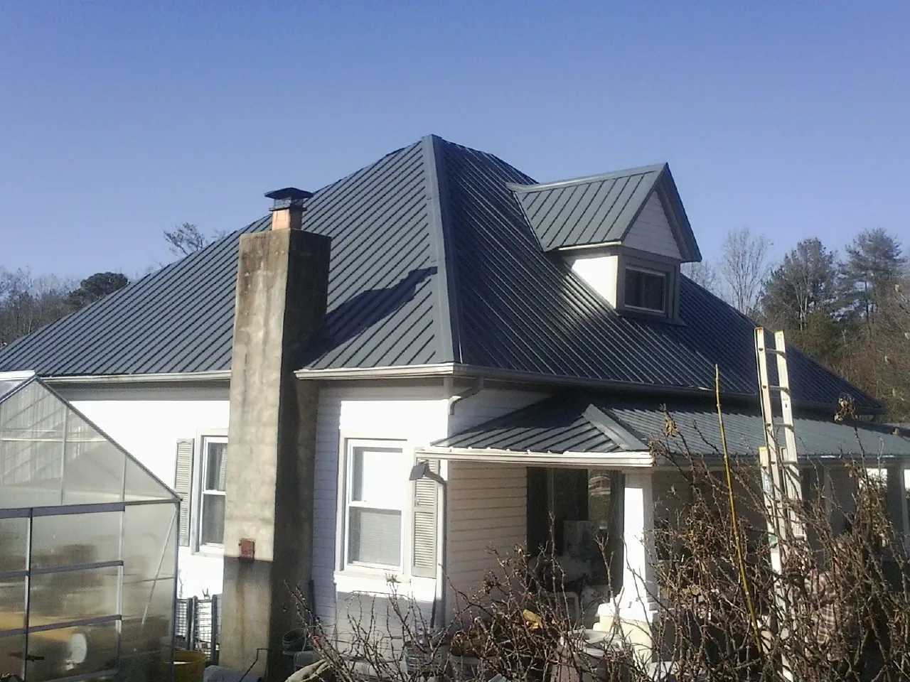 Dark blue standing seam metal roof on a white farmhouse with dormer — Slate & Tile Roof Repair by Roofing Brothers in Manito