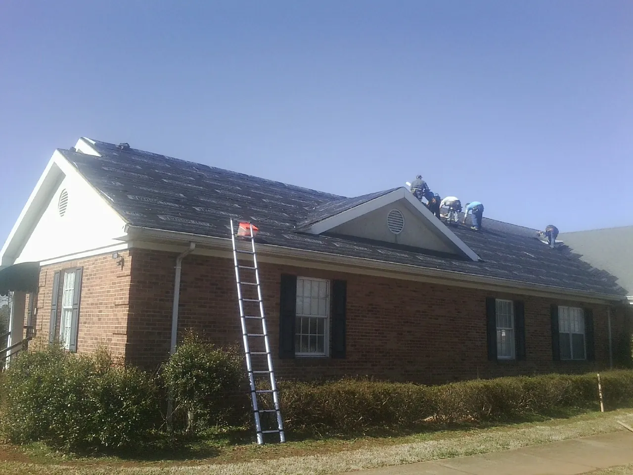 Crew tearing shingles off a brick ranch roof with a ladder set — Emergency Roof Repair work by our crew in Manito