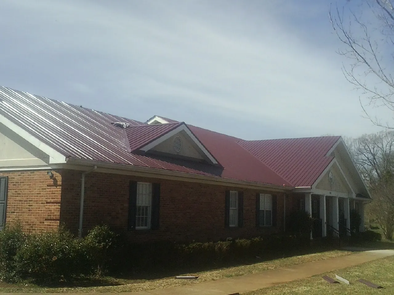 Red metal roof with gabled entries on a long brick building, from a Hail Damage Roof Repair job in Manito