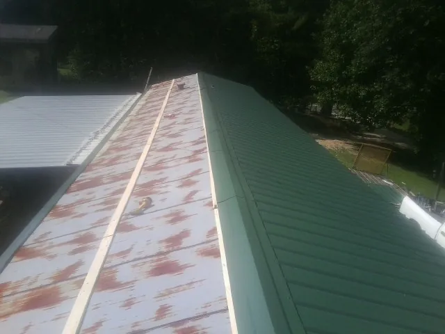 Old rusted panels beside newly installed green metal roofing — Wind Damage Roof Repair by Roofing Brothers in Manito