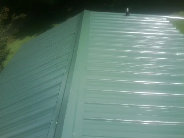 New green metal panels meeting at the ridge of a roof — Flat Roof Repair work by our crew in Manito