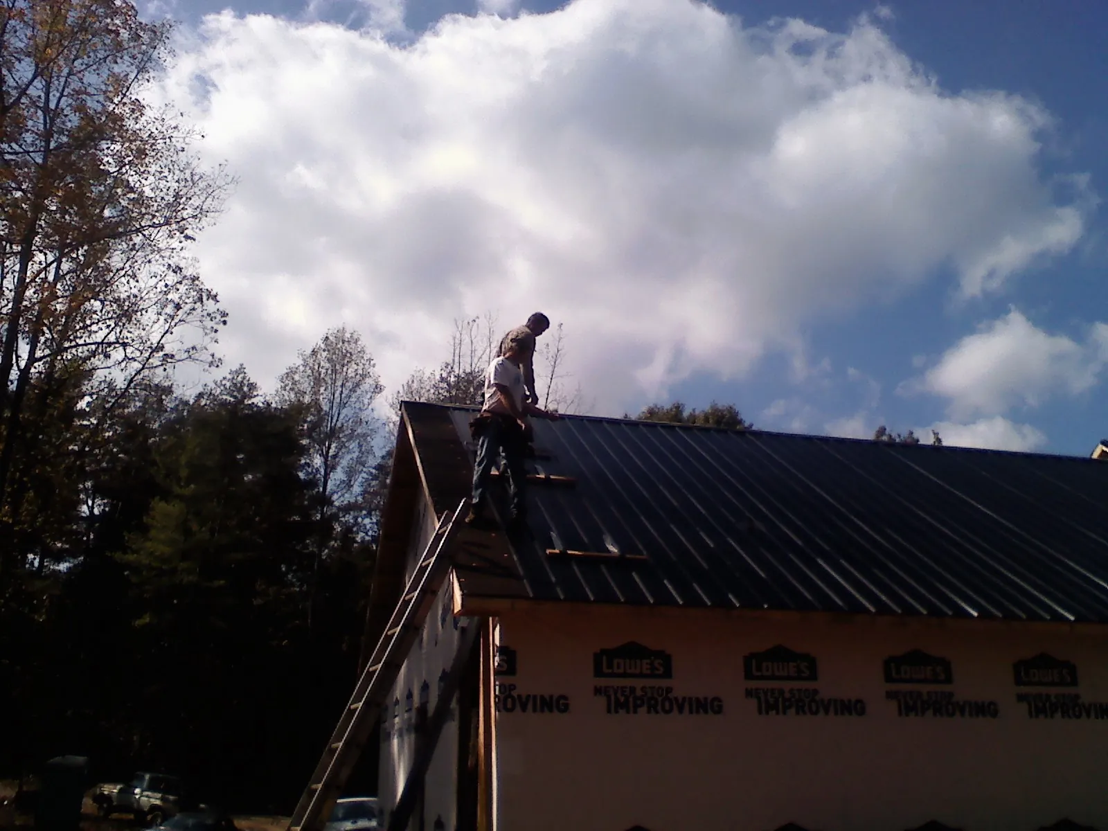 Roofer fastening dark metal panels high against a cloudy sky, from a Roof Inspection job in Manito