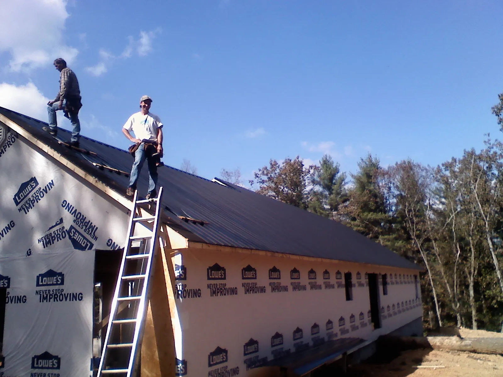 Two roofers standing on a long dark metal roof over a wrapped building in Manito